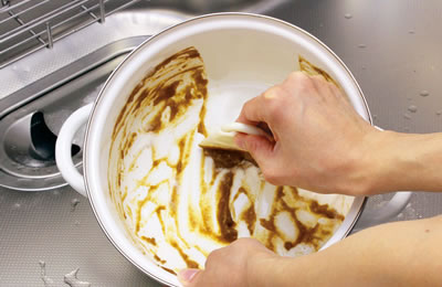 カレー鍋の汚れをスクレーパーで拭き取る